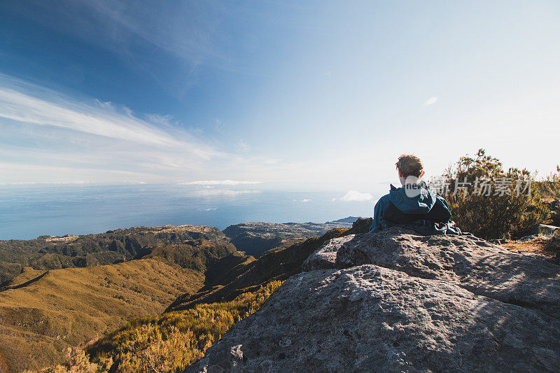 金发旅行者在一块岩石上休息，俯瞰大西洋和马德拉山谷的山坡上的Pico Ruivo葡萄牙岛。坐下